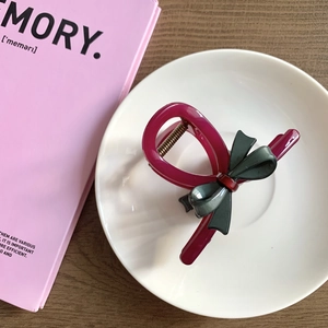 Detailed view of acetate bow hair claw clip in dark pink and green contrast on a plate