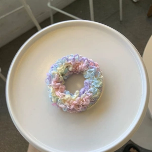 Handgefertigter Häkel-Haargummi in Pastellfarben auf einem weißen Präsentationsteller