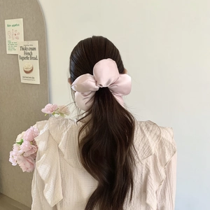 Vue détaillée d'un chouchou noeud en satin rose pâle porté sur les cheveux d'un modèle