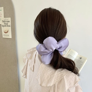 Gros plan d'un chouchou noeud géant en satin violet porté sur une queue de cheval