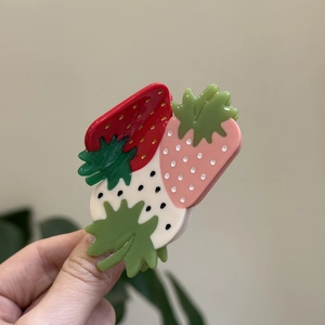 Vue détaillée d'une pince à cheveux fraise en acétate rouge et rose tenue à la main