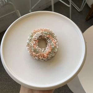 Detailansicht eines gestrickten Blumen-Haargummis mit pastellfarbenen Spitzenrüschen