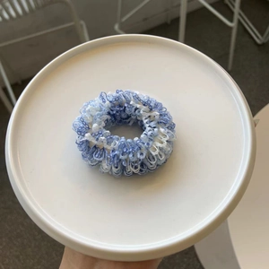 Detailansicht eines blau-weißen plissierten Haargummis im Boho-Stil auf weißem Teller