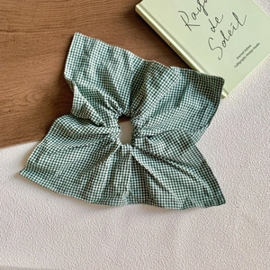 Close-up of green and white gingham fabric scrunchie with large bow detail on wooden surface