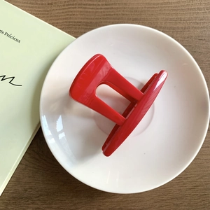 Gros plan d'une pince à cheveux en résine rouge brillant sur une assiette blanche épurée