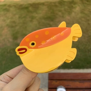Pince à cheveux crabe en forme de poisson-globe jaune avec des taches orange sur l'herbe