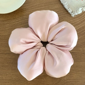 Détail d'un grand chouchou fleur en satin rose clair avec texture soyeuse et pétales