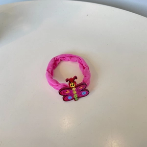 Rosa Samthaargummi mit bunt gepunktetem Acryl-Schmetterling auf weißem Hintergrund