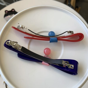 Dettaglio di fermagli a molla in acetato con fiocchi e perline rosse e viola