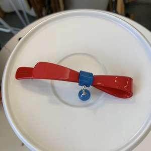 Dettaglio del fermaglio a fiocco rosso con ciondolo a perla blu e scritte incise