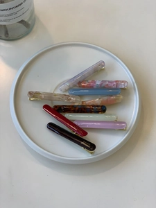Detailed view of elegant acetate hair clips with marble patterns in a white ceramic dish