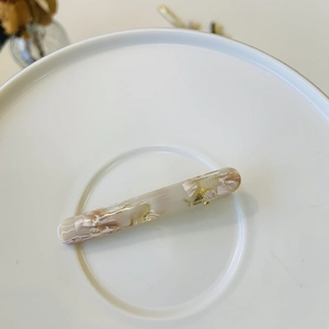 Detail showing marble texture resin hair clip with gold metal base and Barrette text