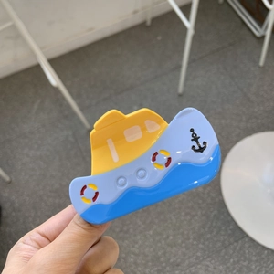 Détail d'une pince à cheveux en acétate en forme de bateau avec ancre et bouée de sauvetage