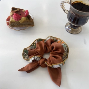 Gros plan d'un chouchou en satin marron avec nœud floral sur un bureau blanc