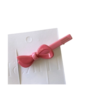 Pink acetate bow hair clip with gold logo detail on high-quality white display card