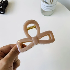 Close-up of nude pink bow hair claw clip showing golden metal spring and acrylic texture