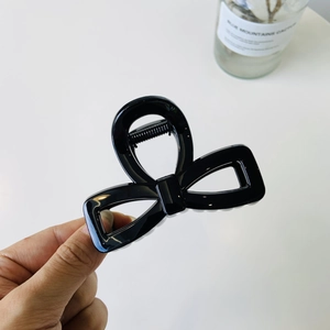 Detailed view of a black glossy bow-shaped hair claw clip held by hand on white background