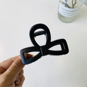 Detail shot of a matte black bow-shaped claw clip with a strong metal spring mechanism