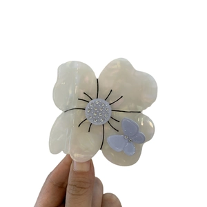 Pinza per capelli a fiore in acetato bianco perlato con farfalla viola e strass in mano