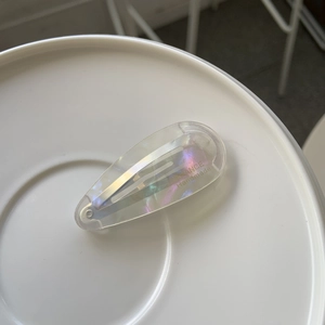 Pince à cheveux goutte d'eau en acétate irisé avec logo France Handmade doré sur fond blanc