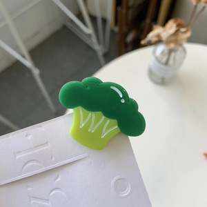 Detail view of a cute acrylic broccoli hair clip with glossy green finish on white board