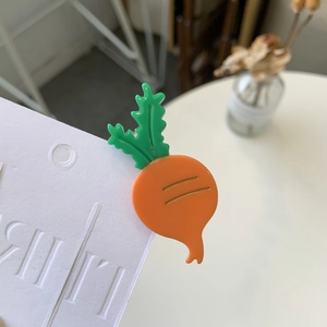 Close-up of a cute orange carrot-shaped acetate hair clip with green leaves on card