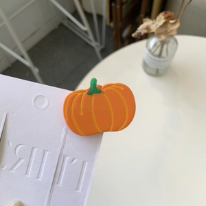 Close-up of a glossy orange pumpkin hair clip on a white decorative card display