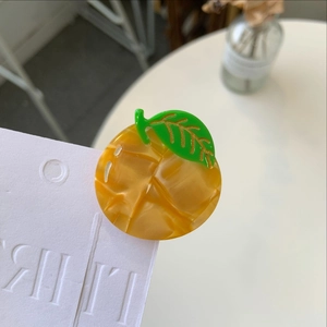 Close-up of a handmade yellow resin mango hair clip with green leaf on a white card