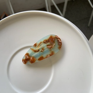 Détail d'une pince à cheveux en acétate marbré bleu et marron avec logo doré
