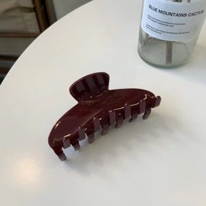Pince à cheveux élégante en résine rouge foncé brillante sur une surface minimaliste