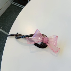 Détail de la pince à cheveux banane avec nœud en résine rose sur matériau translucide