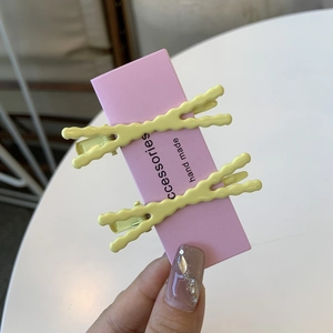 Dettaglio di due fermagli per capelli ondulati giallo brillante su carta rosa