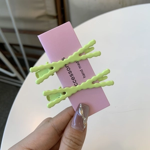 Dettaglio di due fermagli per capelli in metallo verde chiaro su cartoncino rosa