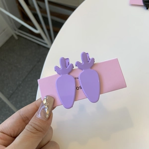 Close-up of two purple carrot-shaped hair clips in glossy finish on a pink display card