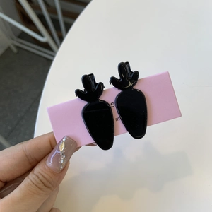 Detail of two black carrot-shaped acetate hair clips on a pink display card