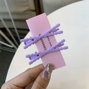 Dettaglio di due fermagli per capelli ondulati viola su un cartoncino di presentazione