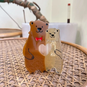 Pinces à cheveux ours en acétate avec motif cœur et nœud sur une surface en osier