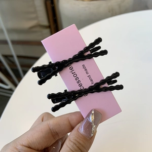 Dettaglio di due fermagli per capelli neri ondulati su un cartoncino rosa in mano