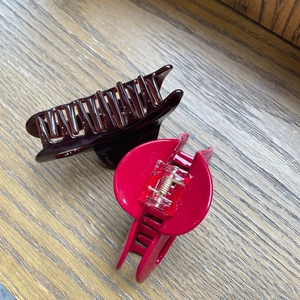 Close-up of acetic acid hair clips in red and brown colors with metal springs on a wood surface