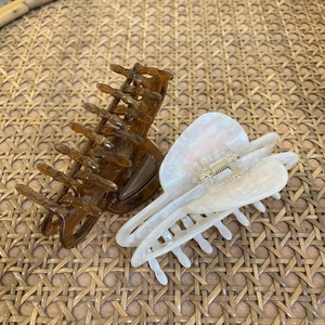 Detailed view of amber and pearl white acetate hair claws with multi-tooth metal spring