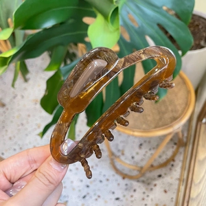 Brown acetate hair claw clip with vintage texture shown in a hand-held lifestyle view