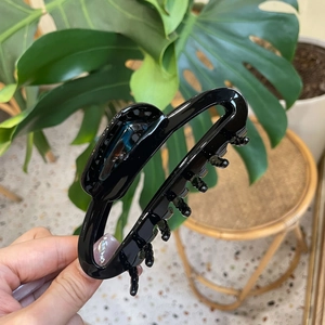 Close-up of a large black acetate hair claw clip held by hand in a natural setting