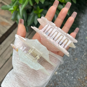 Close-up of pink and white acetate swan hair claws with floral detail held by hand