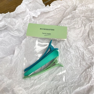 Detailed view of three green matte duckbill hair clips on white paper packaging