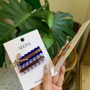 Close-up of blue plaid and solid hair clips on white card with green plant background