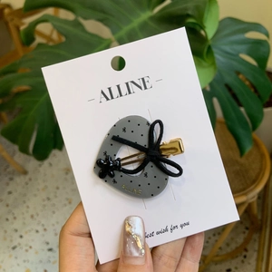 Pince à cheveux grise en forme de cœur avec nœud noir et pois sur sa carte