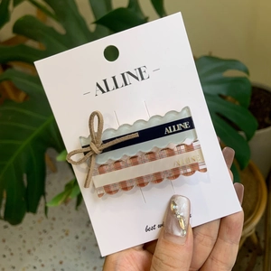 Blue bow hair clip and plaid duckbill hairpin set on a white display card with greenery
