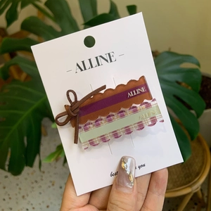 Set of 2 acrylic plaid and bow hair clips on display card with a lifestyle green background