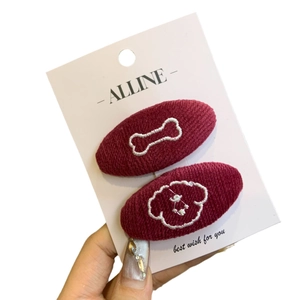 Pair of burgundy knitted hair clips featuring white stitched dog and bone patterns on a card