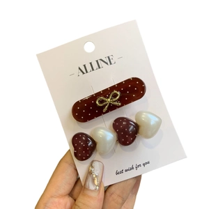 Handheld view of two sweet burgundy and white heart pattern and polka dot bow hair clips